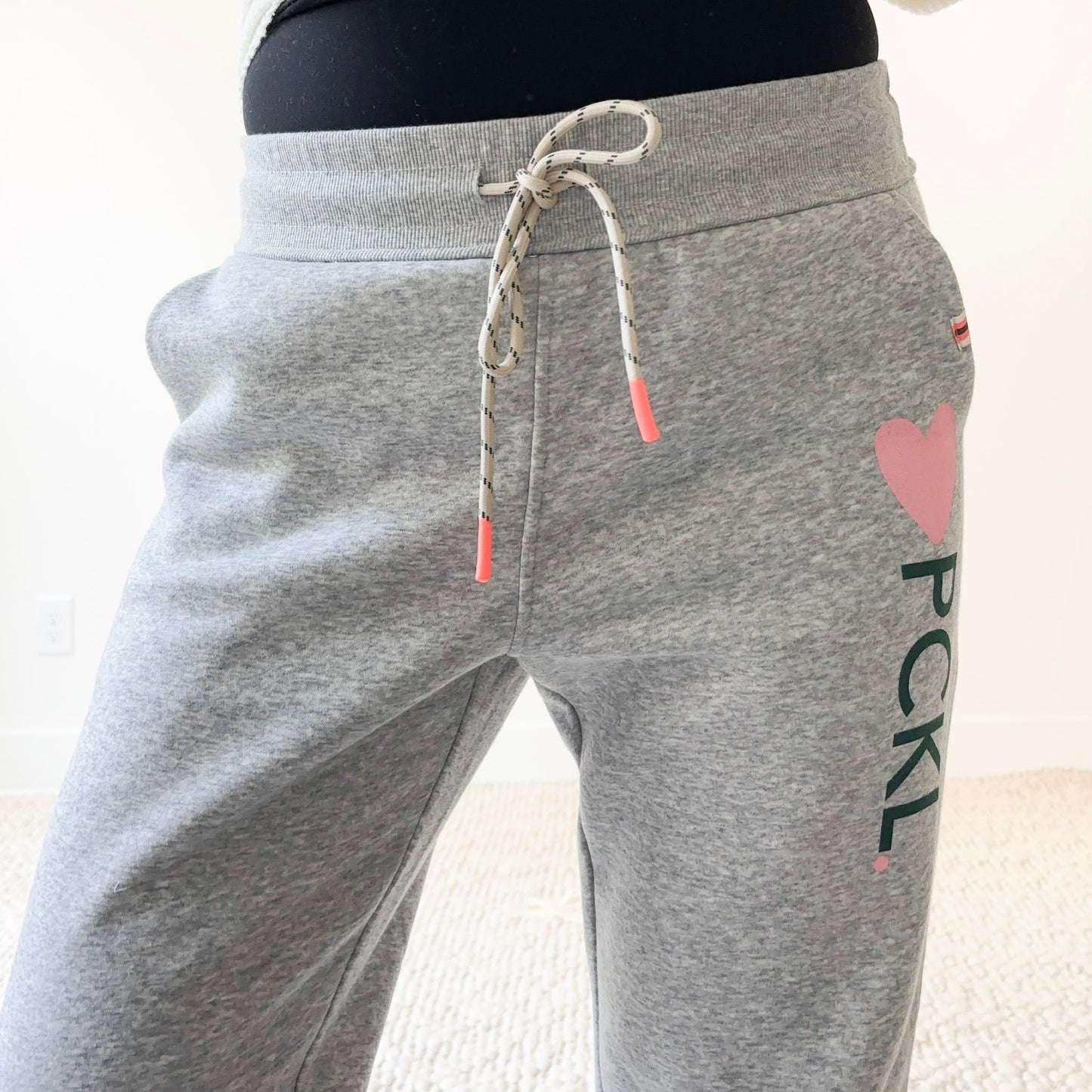 Women's light heather grey slim fit fleece jogger with pink heart and dark green pckl pickleball print.