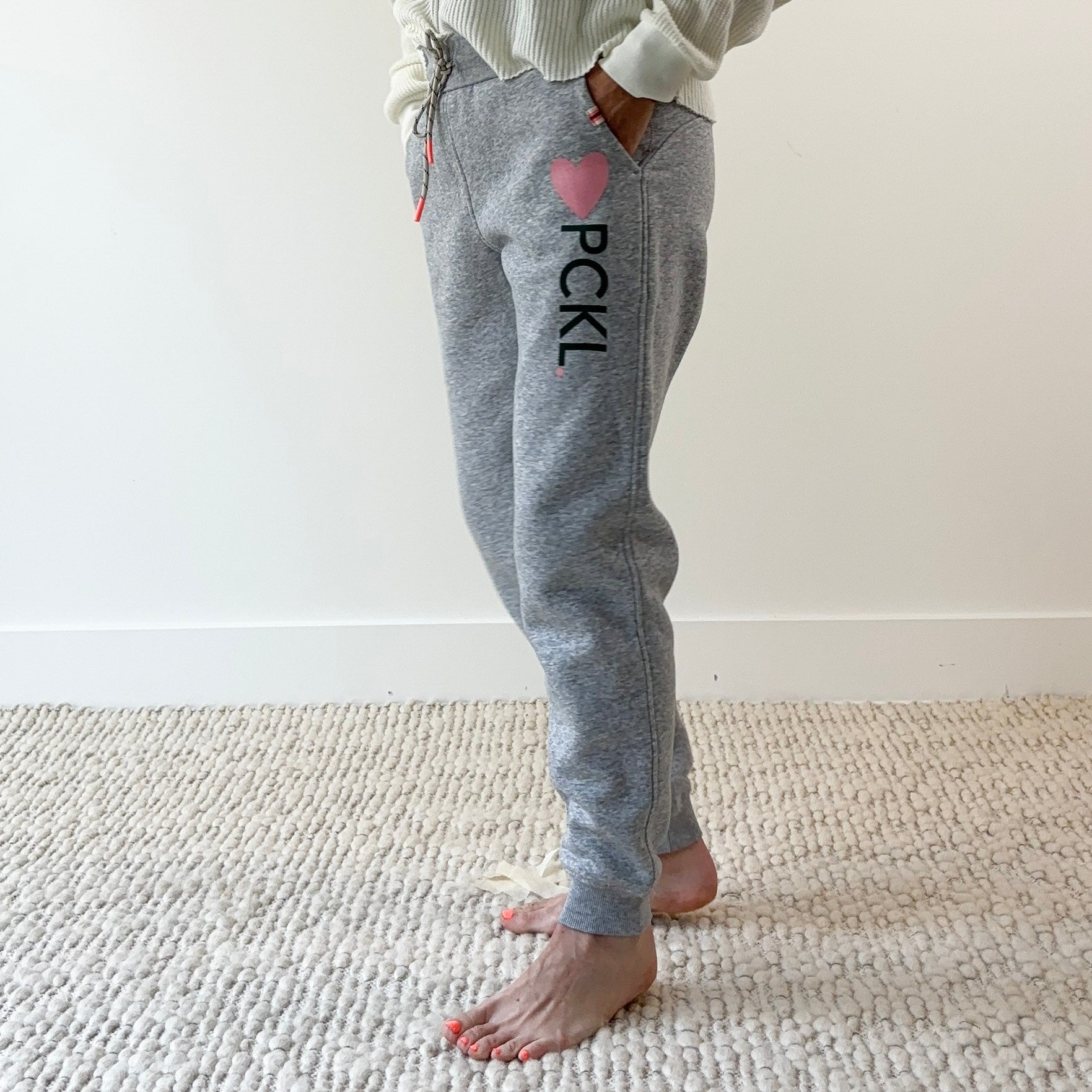 Women's light heather grey slim fit fleece jogger with pink heart and dark green pckl pickleball print.