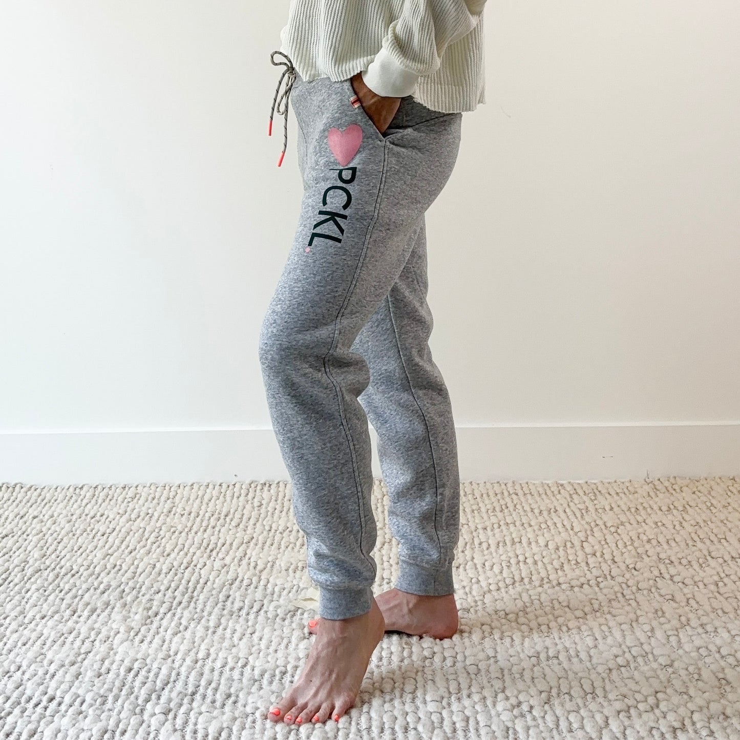 Women's light heather grey slim fit fleece jogger with pink heart and dark green pckl pickleball print.  