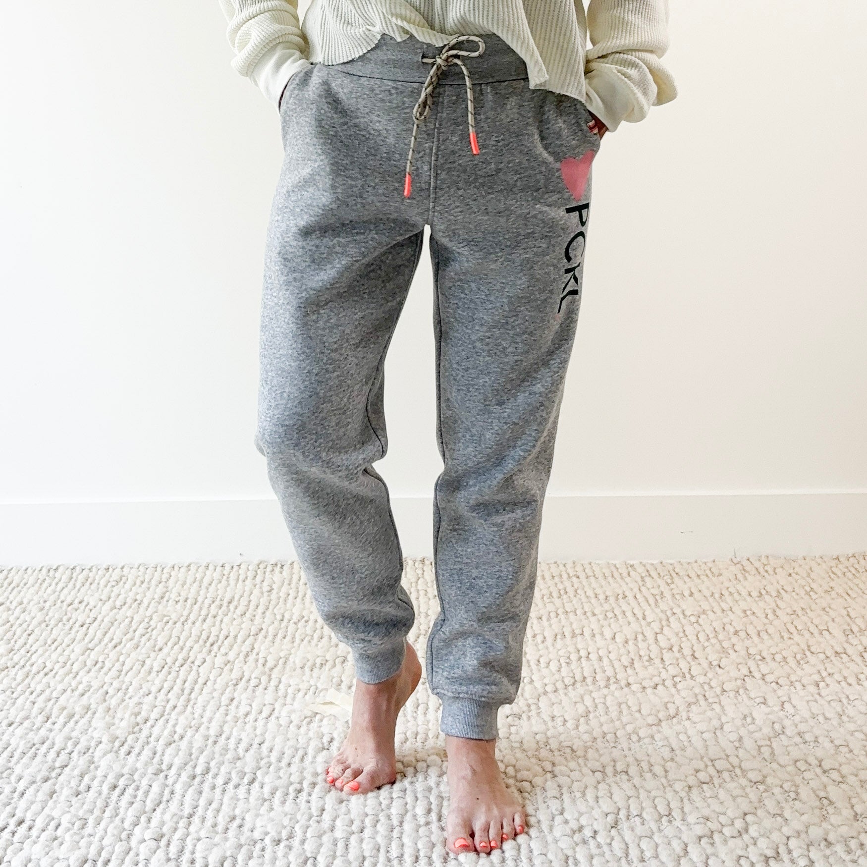 Women's light heather grey slim fit fleece jogger with pink heart and dark green pckl pickleball print.